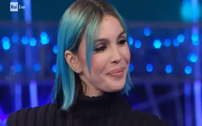 Una donna con capelli blu e neri, trucco marcato, sorride con un'espressione da rose villain.