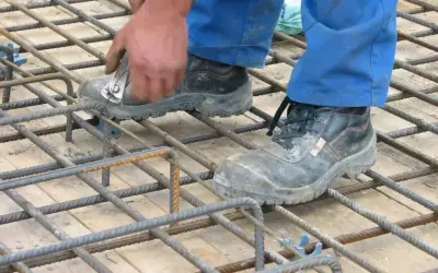 Pracownik w niebieskich spodniach i roboczych butach wiąże zbrojenie pod strop monolityczny.