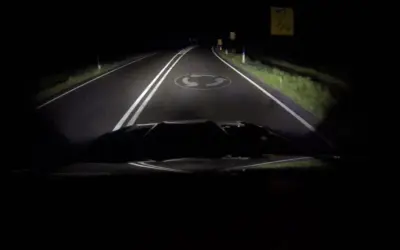 La route de nuit, éclairée par les feux de route, révèle un rond-point.