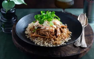 En tallrik med pulled pork med ris, toppad med krispig coleslaw och gröna blad. En härlig måltid som ser utsökt ut.