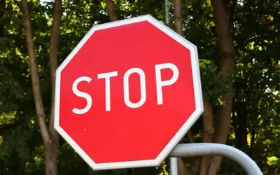 Ośmiokątny, czerwony znak stop z białym napisem "STOP" na tle zielonych drzew.