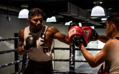 A boxer throws a powerful left hook in a boxing ring, his opponent ready to block.