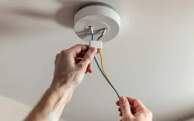 Mains électriques connectées pour installer un plafonnier. Les fils colorés sont manipulés avec soin.