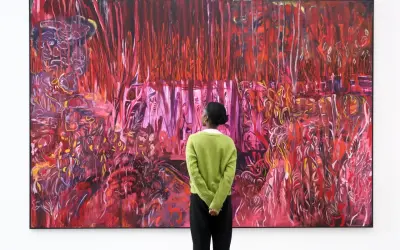 A person in a green sweater contemplates a vibrant, abstract painting, a visual guide on how to find up and coming artists.