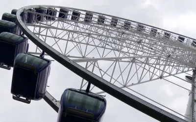 Widok z dołu na koło widokowe w Gdyni z ciemnoniebieskimi gondolami.