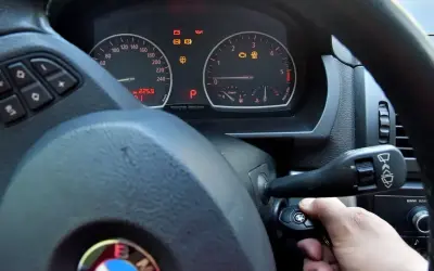 Ręka przekręca kluczyk w stacyjce BMW. Kontrolki na desce rozdzielczej świecą, ale rozrusznik nie kręci tylko cyka.