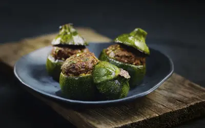 Trois courgettes rondes farcies, garnies d'une préparation savoureuse, reposent sur une assiette sombre, posée sur un plateau en bois vieilli.