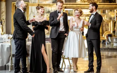 Eleganckie kobiety w sukniach wieczorowych i mężczyźni w garniturach, zgodnie z dress codem black tie, wznoszą toasty.