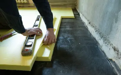Ręce układają żółty styropian pod wylewkę, używając poziomicy. Unikaj błędów przy układaniu styropianu pod wylewkę.