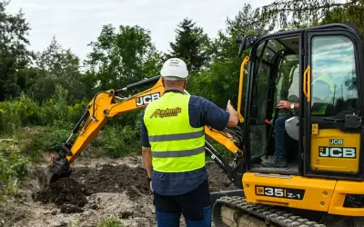 Instruktor z Akademii Operatora pokazuje, ile kosztuje godzina pracy koparki JCB. Operator w kabinie.