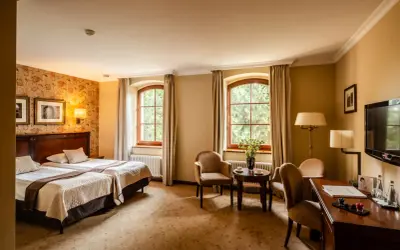 Przytulny pokój hotelowy z dwoma łóżkami, dwoma oknami i widokiem na zieleń. Idealne miejsce na wypoczynek po zwiedzaniu Wrocławia, Zamek Topacz czeka!