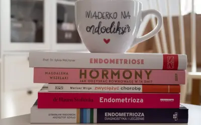 Stos książek o endometriozie, w tym "Endometrioza: diagnostyka i leczenie", z kubkiem "Wiaderko na endoeliksir".