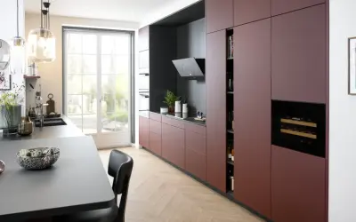 Cuisine moderne avec des armoires bordeaux allant jusqu'au plafond, un îlot central gris, et une grande fenêtre lumineuse.