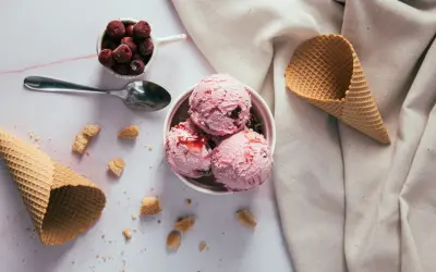 Schüssel mit rosa Eiskugeln, Kirschen und Waffelhörnchen. Ein süßer Genuss, der trotz der Kalorien verlockt.