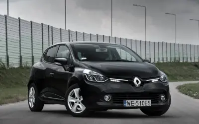 Czarny Renault Clio IV na drodze, z barierą dźwiękochłonną w tle.