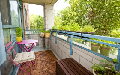 Zielony balkon z meblami i roślinami. Jak osłonić balkon w bloku? Rośliny na balustradzie i drewniana podłoga dodają uroku.