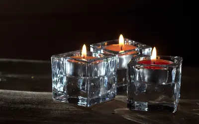 Trzy szklane świeczniki z płonącymi świecami, oświetlone ciepłym blaskiem, jak podczas złotej godziny.