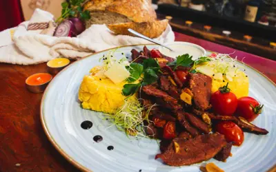 Pyszne jedzenie w Rumunii: polenta z wołowiną, pomidorkami i serem. Obok świeży chleb i świece tworzą przytulną atmosferę.