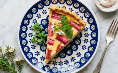 Pyszna tarta rabarbarowa z kremowym nadzieniem, udekorowana miętą i kwiatkami, na talerzu w tradycyjne wzory.