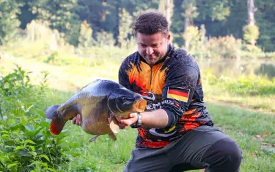 Wędkarz z dumą prezentuje okazałego karpia, który z pewnością nie jest ani sieją, ani sielawą.
