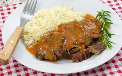 Deliciosa lengua en salsa con arroz blanco y una ramita de romero. Un plato reconfortante listo para disfrutar.