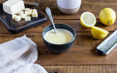 Un bol de sauce beurre citron, avec des citrons, du beurre coupé en dés et une râpe à zester sur une table en bois.