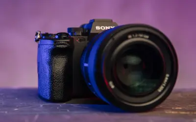 Czarna lustrzanka z kamerą Sony, z obiektywem na pierwszym planie, oświetlona niebieskim i fioletowym światłem.