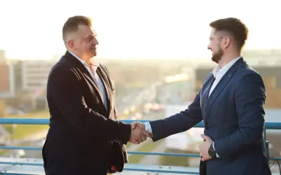 Dwóch mężczyzn w garniturach ściska sobie dłonie na tle miasta.