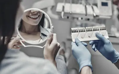 Stomatolog porównuje odcień zębów pacjentki z wzornikiem w gabinecie dentystycznym.