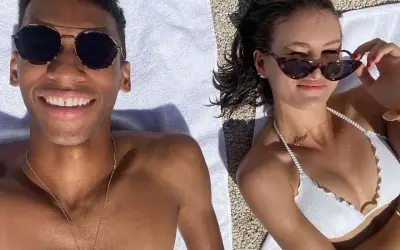 Felix Auger-Aliassime y su novia disfrutan del sol en la playa. Él sonríe a la cámara, ella se ajusta las gafas de sol.