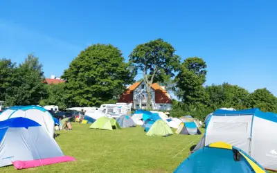 Łowisko wędkarskie i pole namiotowe Zofia i Waldemar Demscy. Wiele namiotów na zielonej trawie, w tle dom i drzewa.
