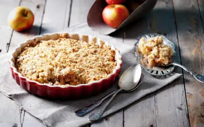 Un délicieux crumble aux pommes tout juste sorti du four, servi dans un plat rouge, avec une portion sur une cuillère ornée.