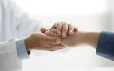 Lekarz w białym fartuchu trzyma za rękę pacjenta.
