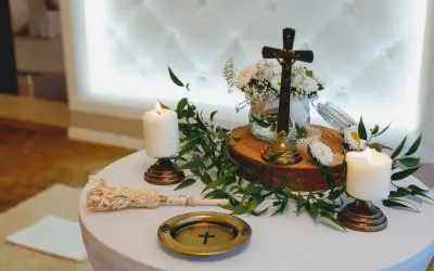 Stół na błogosławieństwo z krzyżem, świecami i bukietem białych kwiatów.