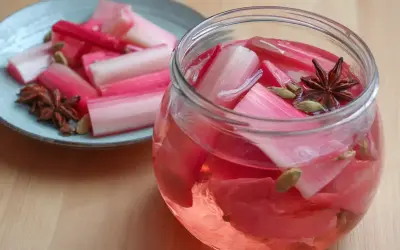 Rabarbersaft recept: färska rabarberbitar i en glasburk med kryddor som stjärnanis och kardemumma. En tallrik med rabarber och kryddor står bredvid.