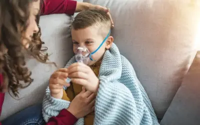 Chłopiec z maseczką nebulizatora, otulony kocem, czuje się jakby dopadła go klątwa Ondyny. Mama czule go głaszcze.