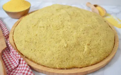 Gotowa, puszysta polenta na drewnianej desce, obok miseczka z mąką kukurydzianą.