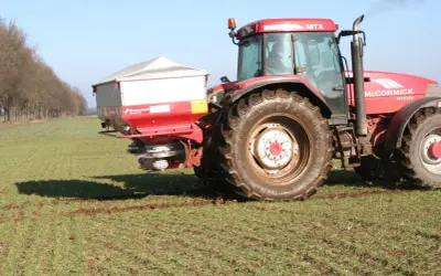Czerwony traktor McCormick MTX 185 z rozsiewaczem nawozów, który właśnie rozprowadza **nitrabor** na polu.