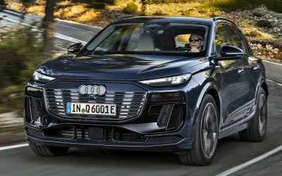 Ciemnogranatowy Audi Q6 e-tron jedzie po krętej drodze. Sprawdź atrakcyjną audi q6 e-tron cenę.
