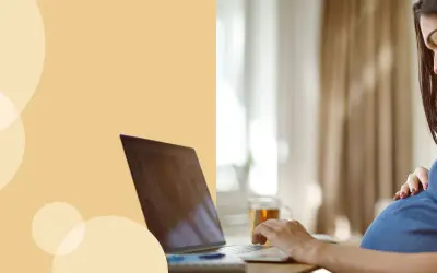 Kobieta w ciąży przy laptopie, która uśmiecha się, dotykając brzucha. Dowiaduje się, jak liczyć ruchy dziecka.