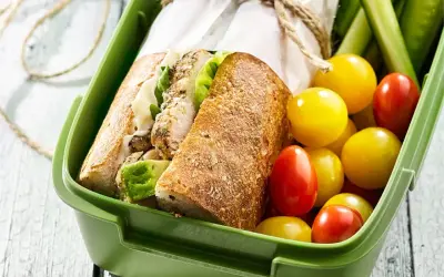 Pyszna kanapka z kurczakiem, świeże pomidorki i ogórek w zielonym pudełku na lunch.