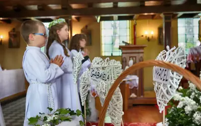 Dzieci w bieli czekają na komunię. W koszyku serca z imionami Marcel i Gabriela.
