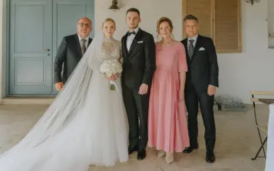 Para weselna z rodzicami. Panna młoda w sukni z welonem, pan młody w garniturze. Obok nich mama weselna w różowej sukience i ojcowie.