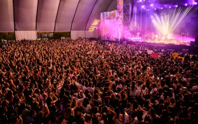 Multitud vibrante en concierto, con luces de escenario y carteles. Se aprecia la **autorización menores espacio Zity** en un cartel.