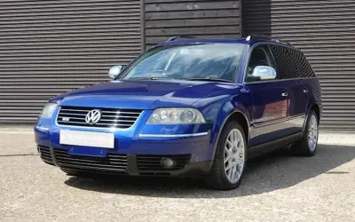 En blå Passat W8 kombi står parkerad framför en träfasad.