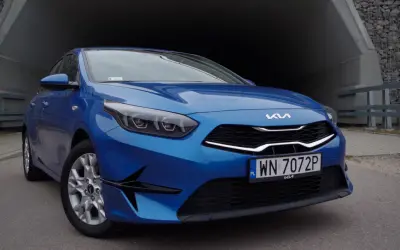 Niebieska Kia Ceed 1.5 T-GDI z nowoczesnymi światłami i grillem, zaparkowana przy betonowym tunelu.