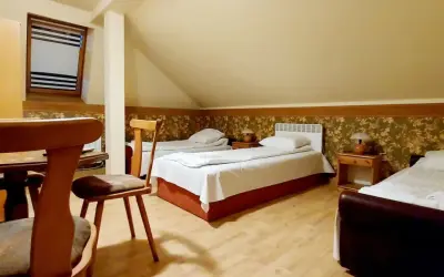 Pokój z trzema łóżkami, stolikami nocnymi i lampkami. W tle okno z żaluzjami. Wygodnie jak w domu w Korczowej.
