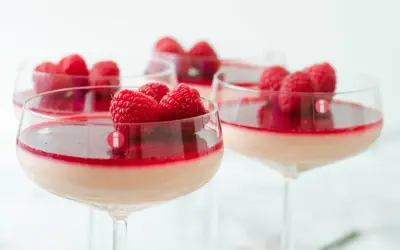 Flera glas med krämig pannacotta, toppad med hallon och en röd sås. En perfekt dessert i glas.