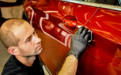 Detailer nakłada powłokę kwarcową czy ceramiczną na błyszczący, czerwony lakier samochodu, dbając o każdy detal.
