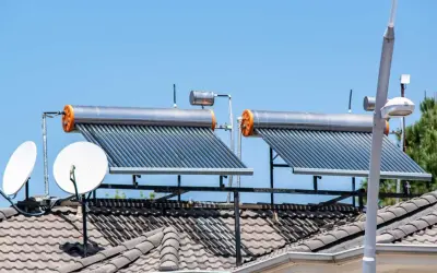 Dos calentadores de agua caliente solar en un tejado, junto a antenas parabólicas, bajo un cielo azul.